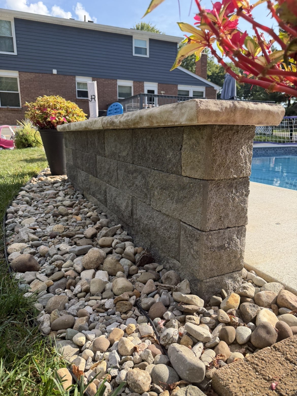 Block retaining wall corner with stone cap by a pool